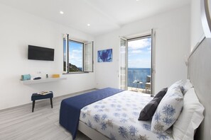 A bedroom with a bed, a TV, a window, and a balcony with a view of the sea.