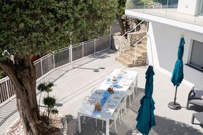 A terrace with a table set for a meal, outdoor seating, and a staircase leading to an upper level.