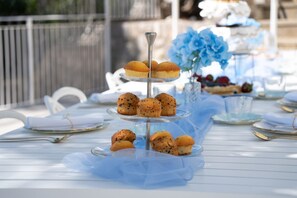 A tiered serving tray with muffins and a glass vase with flowers on a table.