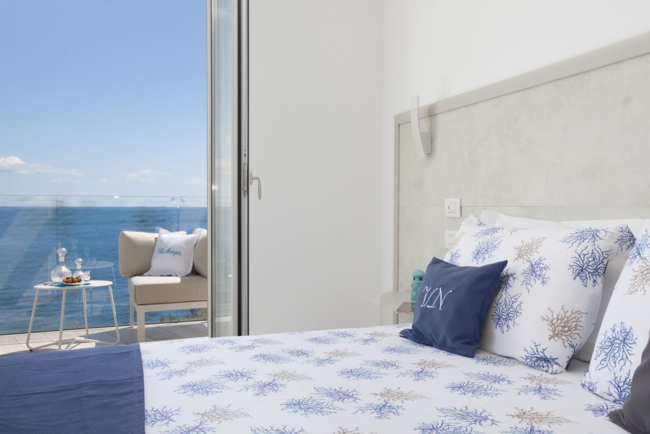 Un dormitorio con cama, almohadas, una mesita de noche, una silla y vistas al mar.