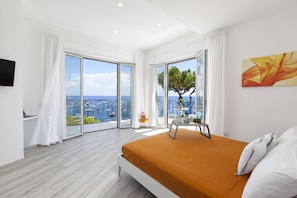 Une chambre avec un grand lit, une vue sur la mer et un balcon équipé d’une table et d’une chaise.