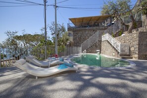 A pool area with a stone wall, a wooden deck, and a metal staircase.