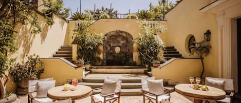 A courtyard with a central stone archway, surrounded by potted plants and outdoor seating with tables and chairs.