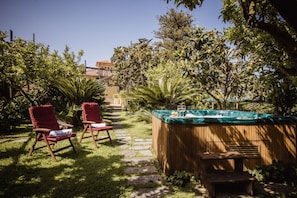 Een tuin met een jacuzzi, twee rode stoelen en een pad van stenen.