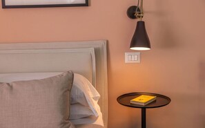 A hotel room with a bed, a bedside table with a book, a wall-mounted light, and a power outlet.