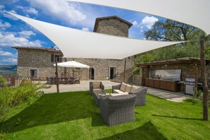 A stone building with a patio area featuring wicker furniture, outdoor seating, and a barbecue setup.
