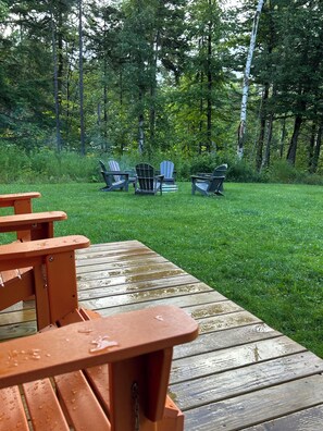 Una terraza de madera con una mesa y sillas de picnic, rodeada de césped y árboles.