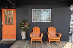 A house with a wooden deck, two wooden chairs, a door, and a wreath.