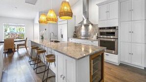 A modern kitchen with a large island, white cabinetry, stainless steel appliances, and pendant lighting.