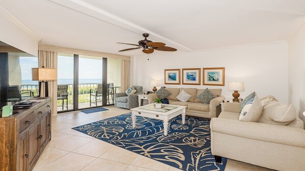 A spacious living room with a balcony, a ceiling fan, and a large window offering a view of the ocean.