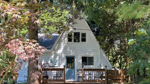 A white house with a gabled roof, surrounded by trees and a wooden fence. - The ‘A’mazing Escape! Beaches, hiking trails, & great fall color tour location! (Manistee)
