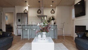 A modern living room with a white coffee table, two black sofas, and a kitchen area in the background. - The Doctors Villa Waikanae (Waikanae Beach)
