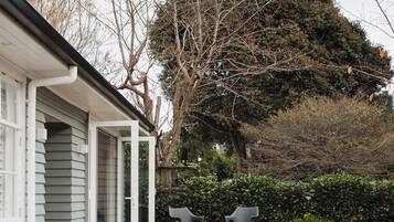 A modern house with a wooden deck, two chairs, and a large tree in the background.