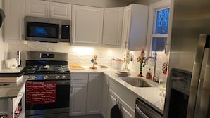 Cozinha com armários brancos, eletrodomésticos de aço inoxidável e janela com vista para árvores.