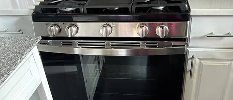 Une cuisine équipée d’une cuisinière, d’un four et d’un plan de travail en acier inoxydable, le tout surmonté d’un comptoir blanc.