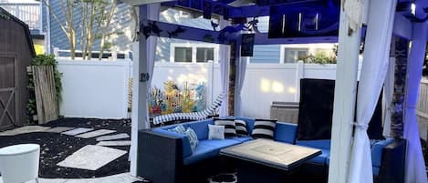 A covered outdoor seating area with a blue sofa and cushions, a small table, and a patterned floor.