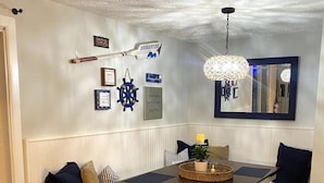 Uma área de refeições com um banco e mesa de madeira, luminária pendente e decorações nas paredes, incluindo um leme de navio e placas emolduradas.