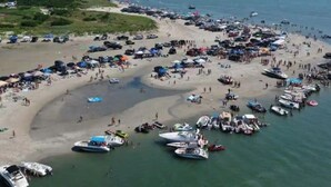 Uma praia com muitos barcos e pessoas, um horizonte urbano ao fundo e um céu claro.