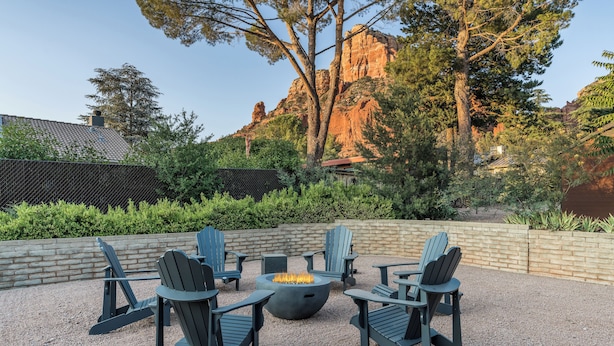 An outdoor seating area with Adirondack chairs and a fire pit, surrounded by a gravel patio and a brick wall.