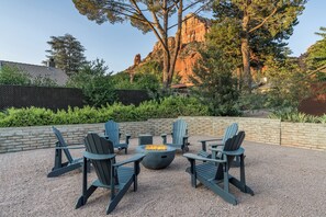 Ein Außenbereich mit Adirondack-Stühlen und einem Feuerkorb, umgeben von einer Schotterterrasse und einer Backsteinmauer.