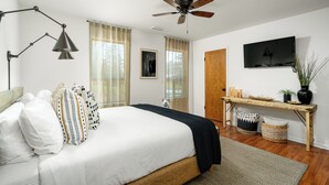 A bedroom with a bed, a desk, a ceiling fan, and a TV on the wall.
