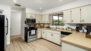 A modern kitchen with white cabinets, stainless steel appliances, and a large window providing a view of the outdoors.