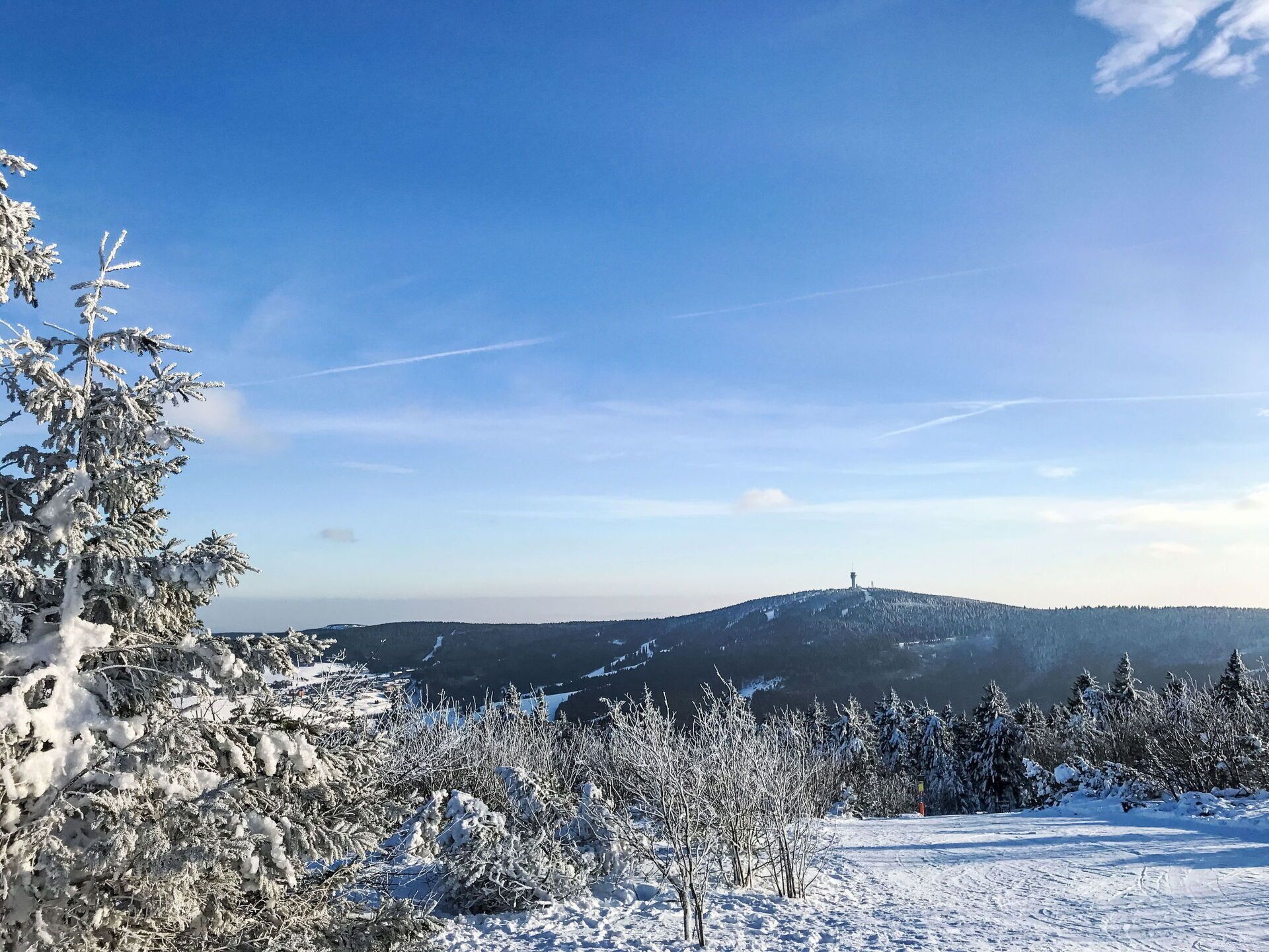 Een besneeuwd landschap met heldere lucht, een berg in de verte en een toren op de heuvel.