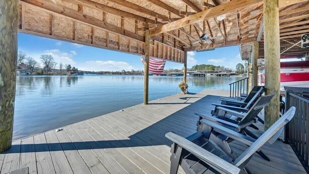 A wooden deck with lounge chairs overlooking a calm lake, an American flag, and a covered area with a view of the water. - Gentle Slope Lakefront beautiful sunset,6Bds,4.5Bas, kayaks,paddleboards,firepit (Moneta)