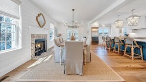 A spacious dining area with a fireplace, a chandelier, and a long wooden table with chairs. - Gentle Slope Lakefront beautiful sunset,6Bds,4.5Bas, kayaks,paddleboards,firepit (Moneta)