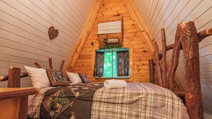 Un dormitorio de cabaña de madera acogedor, con cama, almohadas, una ventana con cortinas y un cartel sobre la ventana.