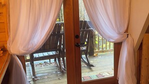 Una cabaña de madera con puerta corrediza de vidrio, cortinas blancas, una terraza de madera y piso alfombrado.