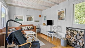 Ein gemütliches Wohnzimmer mit Holzbalkendecke, weißen Wänden, Kamin, Fernseher und Kunstwerken.