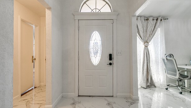 A hallway with a white door featuring a stained glass window, marble flooring, and a chandelier.