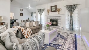 A spacious living room with a fireplace, a ceiling fan, and a dining area in the background.