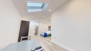 A modern, well-lit room with a skylight, a bed with a blue headboard, and a table with a remote control. - Bicester Court Lodge The Heritage Room | Bicester Holiday Let | 1 Beds & Sleeps 2 (Bicester)
