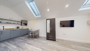 A modern kitchen with grey cabinets, a dining area with a table and chairs, a large wardrobe, and a TV mounted on the wall. - Bicester Court Lodge The Heritage Room | Bicester Holiday Let | 1 Beds & Sleeps 2 (Bicester)
