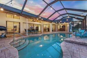 A pool area with a glass enclosure, a dining area, and a view of the sky.