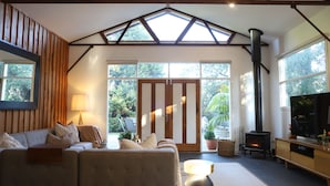 A cozy living room with a sofa, a TV, a fireplace, and large windows. - Barn Stay Hideaway "The Barn" (Somerville)