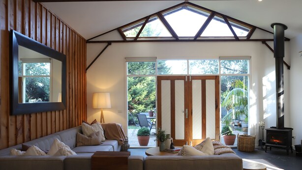 A cozy living room with a sofa, a lamp, a fireplace, and large windows. - Barn Stay Hideaway "The Barn" (Somerville)