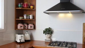 A kitchen with a gas stove, a toaster, a kettle, a shelf with colorful dishes, and a decorative plant. - Barn Stay Hideaway "The Barn" (Somerville)