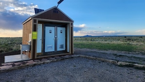 A small, single-story building with two doors, a solar panel on the roof, and a sign indicating a bathroom and parking area.
