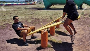 A dinosaur exhibit with a large green dinosaur sculpture and a seesaw.
