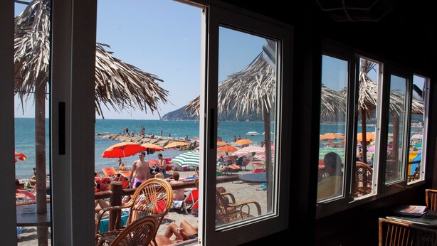 Vista a la playa desde una habitación con ventanas amplias, mostrando sillas y sombrillas de playa.