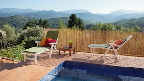 Área de piscina en la azotea con dos sillones de descanso y una mesita, rodeada por una valla de bambú, con vistas a un paisaje montañoso.