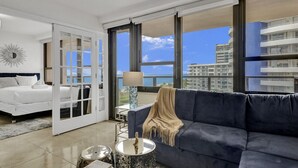 A modern hotel room with a bed, a sofa, a lamp, and a view of the cityscape. - Oceanfront Beach Retreat Beach Service 905 (Miami Beach)