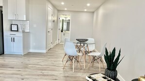 A modern kitchen with white cabinets, a dining area with a glass table and white chairs, and a wooden floor. - Livingston Gem: 5BR Home with Chef's Kitchen (Calgary)