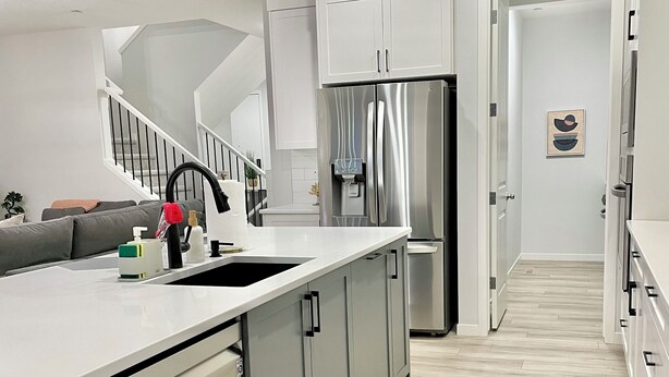A modern kitchen with a stainless steel refrigerator, grey cabinets, and a white countertop. - Livingston Gem: 5BR Home with Chef's Kitchen (Calgary)