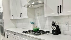 A modern kitchen with white cabinetry, a stainless steel range hood, and a green pot on the stove. - Livingston Gem: 5BR Home with Chef's Kitchen (Calgary)