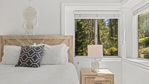 Un dormitorio con cabecera de madera, una mesita de noche con lámpara y vistas a un bosque por la ventana.