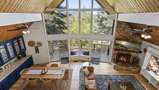 Amplia sala de estar con un ventanal grande, chimenea y comedor, con cocina visible a través de puertas de cristal.